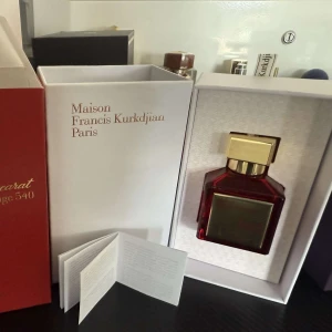 Baccarat Rouge 540 Extrait de Parfum - Lyxig parfym i röd och guld förpackning från Maison Francis Kurkdjian, Paris. Baccarat Rouge 540 Extrait de Parfum är känd för sin intensiva och sofistikerade doft. Kartongen har eleganta gulddetaljer och ett stilrent husmotiv på sidan.