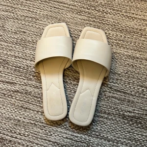 Krämvita sandaler  - Säljer ett par jättefina krämvita sandaler med en lite fyrkantig tå och bred rem. Skorna är köpta från en butik för ett par år sedan men har inte kommit till så mycket användning förutom bara ett fåtal gånger  och är i väldigt bra skick. Den har lite rynkor vilket kommer naturligt på dessa sandaler.🤍