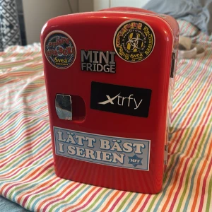 Röd mini kylväska med klistermärken - Säljer en röd mini kylväska med flera klistermärken på utsidan. Väskan har ett handtag upptill och öppnas med en liten kromad lucka. Invändigt är den vit och har plats för mindre drycker eller snacks. Perfekt att ta med på utflykter eller ha på rummet. !Sladd ingår ej!