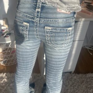 True Religion ljusblå bootcut jeans - Säljer ett par ikoniska ljusblå jeans från True Religion med tydliga vita sömmar och deras klassiska broderade bakfickor. Jeansen har bootcut-modell och är tillverkade i mjukt denim. Perfekta för dig som vill sticka ut med en snygg streetstil. Nypris 2000. Kan tänka mig sälja för mindre. Köpta i USA. Tjejen på bilden är ca 163 och jeansen är lite långa. Hör av er vid frågor:)