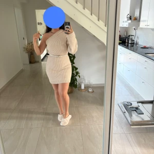 Beige ribbad stickad klänning  - Superfin beige stickad klänning från ginatricot med ribbad struktur och en trendig oneshoulder-design. Perfekt för dig som gillar en unik och stilren look. Klänningen har lång ärm och är mjuk och skön att bära.