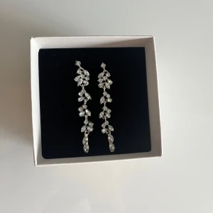 Långa diamant örhängen i silver - Säljer ett par eleganta, långa örhängen i silverfärg med glittrande stenar. Örhängena har ett hängande design med små bladformade detaljer som ger en lyxig och trendig look. Perfekta nu inför bal och liknande🤍