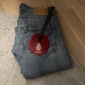 Blå jeans från Dondup - Snygga blå jeans från Dondup med klassisk femficksdesign och läderpatch bak i midjan. Jeansen har en tidlös tvätt och raka ben, perfekta till sneakers eller boots. Materialet är mjukt och slitstarkt denim. Helt nya med tags. Pris är diskuterbart!