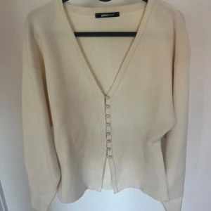 Beige kofta med v-ringning från Gina Tricot - Säljer en beige kofta från Gina Tricot med v-ringning och knappar framtill. Tröjan är stickad och har långa ärmar. Perfekt att slänga på sig över en topp eller klänning. Använd fåtal gånger i storlek S🤍