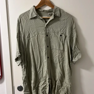 Ljusgrön mönstrad skjorta från Covington - Säljer en ljusgrön skjorta från Covington i storlek L. Skjortan har ett diskret geometriskt mönster, klassisk krage och knäppning framtill. Tillverkad i 100% rayon vilket gör den mjuk och luftig. Perfekt för dig som gillar stilrena detaljer.