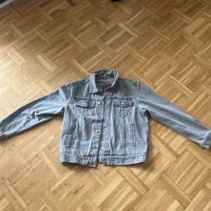 Grå jeansjacka från Denim GenesXCorteiz - Snygg grå jeansjacka från Denim Genes med cool broderad stjärndetalj på ryggen. Klassisk modell med knappar framtill, två bröstfickor och raka ärmar. Perfekt för dig som gillar streetstyle och vill ha en unik touch på din outfit.