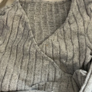 Grå ribbad topp från SHEIN XS - Grå ribbad topp från SHEIN i storlek XS. Toppen har v-ringning och ett diskret randigt mönster i olika grå nyanser. Mjuk och stretchig känsla tack vare materialmixen. Perfekt att styla med jeans eller kjol för en chill look.