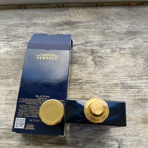Versace Dylan Blue pour Homme 100ml - Versace Dylan Blue pour Homme Eau de Toilette, 100 ml. Flaskan är djupblå i glas med guldiga detaljer och rund Versace-logga framtill. Kommer i en lyxig mörkblå kartong med guldfärgad text och Medusa-symbol. En ikonisk och maskulin doft med elegant design.