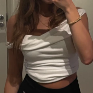 Vit offshoulder croppad topp - Säljer en vit croppad topp med offshoulder-design och snygg drapering över bysten. Toppens passform är tight och den har en stilren look som passar perfekt till höga byxor eller kjol. Materialet känns mjukt och stretchigt, vilket gör den bekväm att bära.
