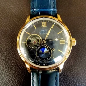 Timex automatisk klocka  - Snygg automatisk klocka från Timex Waterbury Collection med guldig boett, mörkblå urtavla och matchande blått läderband. Urtavlan har öppet hjärta och månfas-detalj, samt romerska siffror i guld. Perfekt accessoar för dig som gillar klassisk men modern stil.