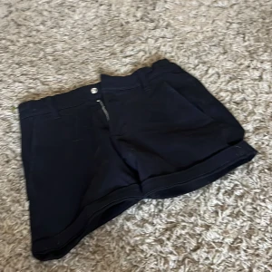 Svarta shorts från 157 med dragkedja - Svarta shorts från 157 med klassisk design, bälteshällor och dragkedja framtill. Shortsen har fickor både fram och bak samt uppvikta benslut. Perfekta för sommardagar och enkel att matcha med allt. Snygg och stilren look.