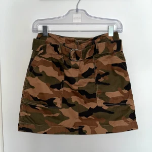 Camo minikjol med bälte - En riktigt snygg kort camouflagemönstrad kjol från Divided By H&M med bälte och silverfärgat spänne. Kjolen har fickor fram och bak samt markerade sömmar. Perfekt för dig som älskar camo! 🤎