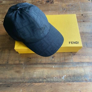 Svart fendi keps  - Snygg svart keps från Fendi med diskret FF-monogram över hela ytan. Kepsen har böjd skärm, justerbar rem baktill i skinn med Fendi-logga perfekt, för dig som vill ha en exklusiv och stilren accessoar. Pris kan diskuteras vid snabb affär. 