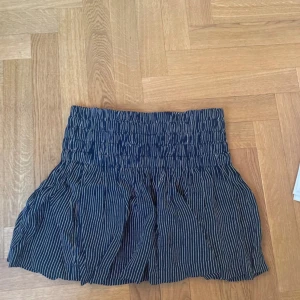 Randig kortkjol från Ganni - Supersöt kortkjol från Ganni i marinblått med vita smala ränder. Kjolen har bred smock i midjan som ger en snygg passform och ett lätt utställt fall. Perfekt för dig som gillar en chill och trendig stil.