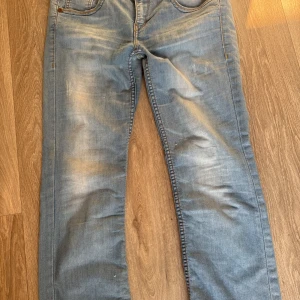Ljusblå jeans från Hilfiger Denim - Säljer ett par ljusblå jeans från Hilfiger Denim med klassisk femficksdesign och snygga slitningar. Jeansen har raka ben och orangea kontrastsömmar. Perfekta för en avslappnad stil.