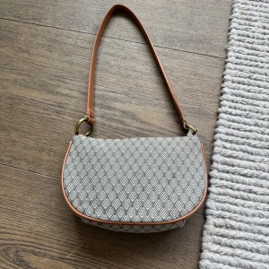 Mönstrad axelväska med bruna detaljer - Säljer min super fina handväska. Mönstretna på väskan är unika och ger en retro känsla. Väskan har dragkedja upptill och kvaliten är bra. Snygg och stilren design som passar till många outfits.