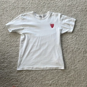 Vit t-shirt från Comme des Garçons Play - Vit t-shirt från Comme des Garçons Play med det ikoniska röda hjärta-trycket på bröstet. Klassisk passform. Använd fåtal gånger, inga defekter. Används inte längre pågrund av att den är för liten för mig. Äkta.