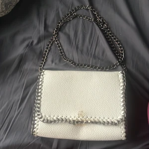 Vit väska  - En vit väska med kedj band knapen som man öppnar väskan med är lite sönder men man kan fortfarande öppna och stänga väskan om man är försiktig.