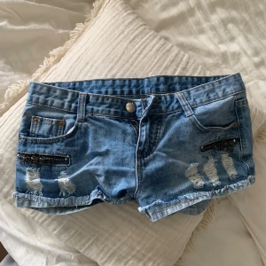 Blå lågmidjade jeansshorts - Säljer ett par blå lågmidjade jeansshorts med slitna detaljer fram och bak. Shortsen är köpta second hand🤍