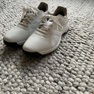 Vita träningsskor från Adidas Traxion - Säljer ett par vita Adidas Traxion golfskof med snörning och svart sula. Skorna har klassisk Adidas-design med diskreta ränder på sidan och är perfekta för golf andvända ungefär 4 gånger men var lite för små
