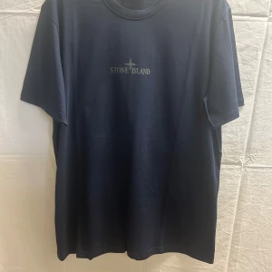 Mörkblå Stone Island t-shirt - Snygg mörkblå t-shirt från Stone Island med klassisk logga tryckt på bröstet. T-shirten har rund halsringning och är tillverkad i mjuk bomull. Perfekt för dig som gillar stilrena och exklusiva plagg med streetkänsla.
