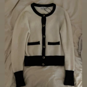  Zara Knit kofta - Snygg vit kofta från Zara Knit med svarta detaljer vid kanter, fickor och knappar. Guldiga knappar framtill ger en lyxig touch. Koftan är stickad och har lång ärm. Liten i storleken så skulle säga det är en Xs/s. passar mig som är 161cm. Fläck på bild 5(går att tvätta bort)
