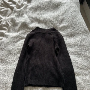 Svart ribbad stickad tröja XS - Svart ribbad stickad tröja i storlek XS. Tröjan har lång ärm och en lite högre halsringning. 
