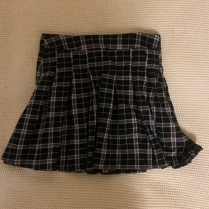 Svartvit rutig plisserad kjol  - Superfin svartvit rutig kortkjol  med plisserad design och dragkedja i sidan. Kjolen har en klassisk midja och är perfekt för en trendig och cool look. Passar dig som gillar grunge/edgy eller streetstyle. Använd en gång.