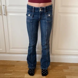 Blå bootcut jeans från H&M utan fickor där bak, storlek 152 - Säljer ett par blå bootcut jeans från H&M med låg midja och justerbar midja. Jeansen har två framfickor  Snygga kontrastsömmar och bekväm passform. 