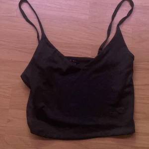 Svart croppad linnetopp från Amisu - Säljer en svart croppad linnetopp från Amisu med smala axelband och v-ringning. Perfekt för sommaren och enkel att matcha med olika outfits. Snygg och stilren design!