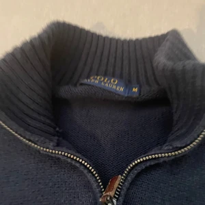 Mörkblå stickad half zip från Polo Ralph Lauren - Säljer en mörkblå stickad tröja från Polo Ralph Lauren i storlek M. Tröjan har en ribbad krage, half zip-dragkedja och det klassiska röda broderade logot på bröstet. Perfekt för lager-på-lager och chill stil.