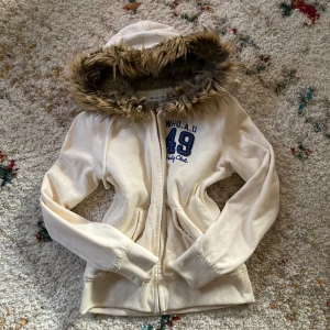 Fur hoodie - Mysig vit furhoodiw från WHO.A.U med huva och fuskpäls runt kanten. Jackan har dragkedja, broderad blå logga på bröstet samt två fickor framtill. Insidan är fodrad! Storlek L men passar från S beroende på hur man vill att den ska sitta♥️ litet hål längst ner (se sista bilden) 