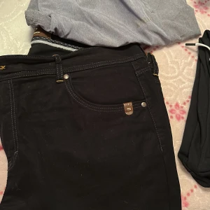 Svarta jeansbyxor från G-Star - Säljer ett par svarta jeansbyxor från G-Star med klassisk femficksdesign och silverfärgade nitar. Byxorna har normal passform och är tillverkade i ett slitstarkt jeanstyg. Perfekta för dig som gillar stilrena och tidlösa jeans.