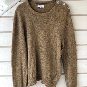 Wolsey, stickad tröja, storlek L - Gul/brunmelerad tröja med dekorativa knappar på axeln. Rund halsringning och ribbstickade muddar. Använd en gång och i nyskick.