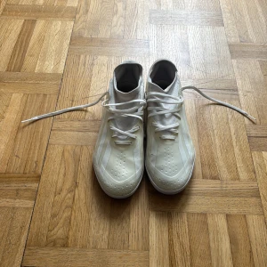 Vita adidas fotbollsskor med snörning - Snygga vita fotbollsskor från adidas med klassiska tre ränder på sidan. Skorna har snörning, rund tå och perforerade detaljer framtill för extra ventilation. Perfekta för dig som vill sticka ut på planen med stilrena och fräscha skor.