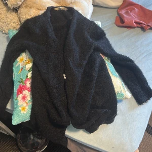 Svart halv fluffig kofta från H&M använd ett antals gånger - Mysig svart kofta från H&M i storlek 122/128. Koftan är fluffig och har en öppen front utan knappar, perfekt att slänga på sig när det är kyligt. Långärmad och i ett mjukt, stickat material som känns skönt mot huden.