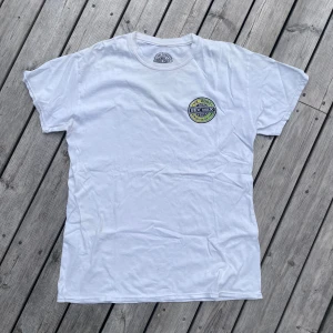 Vit t-shirt från Mr. Zog's Sex Wax - Riktigt fett Vit t-shirt från Mr. Zog's Sex Wax med rund hals och tryck både fram och bak. Stort färgglatt logotryck på ryggen och mindre logga på bröstet. Tillverkad i 100% bomull för en skön och klassisk känsla. Skriv gärna vid funderingar🔥