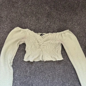 Ljusgrön offshoulder topp  - Säljer en ljusgrön offshoulder topp från Bik Bok i storlek S (passar även XS). Toppen är croppad med långärmade ärmar och har smockat tyg som ger en snygg och bekväm passform. Perfekt för dig som gillar trendiga och feminina plagg!