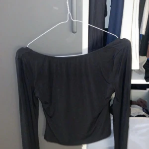 Svart offshoulder topp - Trendig svart offshoulder topp med långa ärmar. Snygg och enkel design som passar perfekt till många olika outfits. Mjuk och stretchig känsla i materialet.