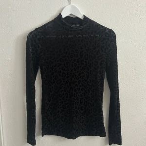 Svart leopardmönstrad topp från Mango - Snygg svart långärmad topp från Mango med leopardmönster. Tight passform och hög hals, tillverkad i ett stretchigt och glansigt syntetmaterial som ger en cool look.💕