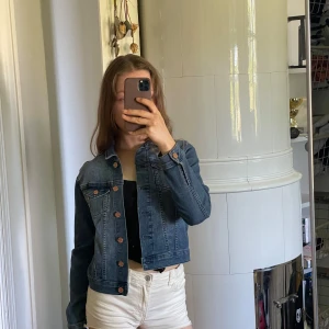 Klassisk blå jeansjacka från &Denim - Säljer en klassisk blå jeansjacka från &Denim med bruna knappar och två bröstfickor. Jackan har en tidlös design, raka linjer och lång ärm. Perfekt att slänga över en topp eller hoodie nu på sommaren. Har en annan som är lite mer oversized som jag använder mer haha.