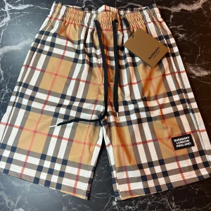 Rutig shorts från Burberry - Snygga shorts från Burberry med klassiskt beige, svart, vitt och rött rutmönster. De har elastisk midja med svart snörning och en liten Burberry-logga på benet. Perfekta för sommaren och ger en lyxig känsla till din outfit.