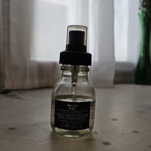 Davines OI Oil - En genomskinlig glasflaska med pump, innehållande Davines OI Oil. Oljan är lätt gulaktig och används för att ge glans och mjukhet till håret. Flaskan rymmer 50 ml och har en svart etikett samt svart pump med genomskinligt lock. Ca hälften kvar, perfekt om du funderar på att köpa en stor men först vill testa oljan under ett tag