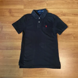 Svart pikétröja från Polo Ralph Lauren - Säljer nu denna svarta pikétröja från polo Ralph Laurent! Den har blivit lite solblekt sedan förra sommaren och lite vitare fläckar efter jag strykt den men borde gå bort lätt i tvätten, men annars inga andra defekter. Storleken är 14-16 år vilket motsvarar ungefär XS! Vid fler frågor eller liknande kom privat! // Levi
