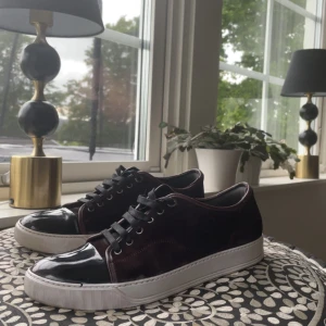 Lanvin vinröda - Säljer ett par svarta sneakers från Lanvin med snygg lackad tå och vita sulor. Skorna har svarta skosnören och ovandel i mocka. Klassisk och stilren design som passar till mycket. Skorna är i bra skick men fixade med whitening cream på sulan! Tveka inte på att fråga frågor! Priset är ej hugget i sten. 