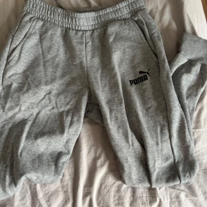 Grå mjukisbyxor från Puma - Säljer ett par klassiska grå mjukisbyxor från Puma med resår i midjan och vid bensluten. Byxorna har sidofickor och Puma-logga tryckt på vänster ben. 