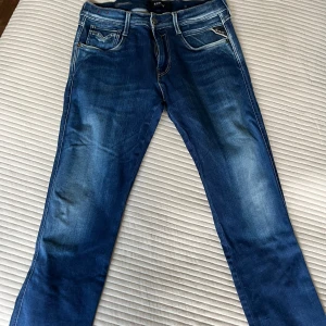 Replay Hyperflex jeans blå, W29 L32 - Snygga blå Replay Hyperflex jeans med klassisk femficksdesign och stretchigt material. Jeansen har en något tvättad look och raka ben. Perfekta för dig som vill ha både stil och komfort i vardagen.