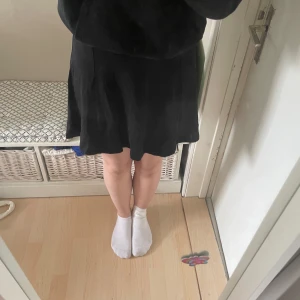 Svart kortkjol i bomull - Enkel och stilren svart kortkjol med lätt utställd passform. Kjolen är sydd i ett mjukt bomullstyg och har en klassisk midja utan synliga detaljer. Perfekt att matcha med olika toppar för en clean look.