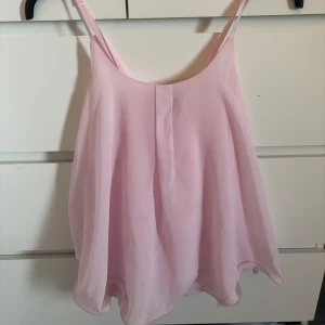 Ljusrosa linnetopp med lös passform - Säljer en ljusrosa linnetopp med tunna axelband och lös, fladdrig passform. Toppen har en lätt och luftig känsla, perfekt för varma dagar. Enkel och stilren design som passar till många olika outfits.
