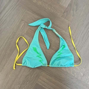 Blå och gul bikiniöverdel från Diesel - Snygg bikiniöverdel från Diesel i blått med gula knytband och gröna detaljer framtill. Klassisk trekantsmodell med knyt i nacken och ryggen. Perfekt för stranden eller poolen. Passar m också!Pris går jättebra att diskuteras